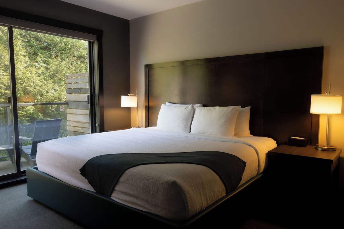 Een moderne hotelkamer met een groot bed, twee bedlampen en uitzicht door een schuifdeur.