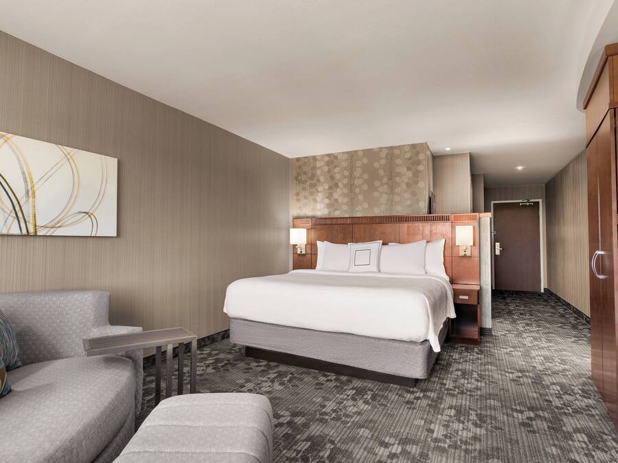 Una habitación de hotel con una cama grande, un sofá, una mesita y un armario.