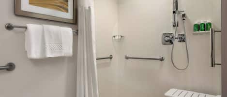 Un baño con ducha, un tendedero blanco para toallas, una obra de arte enmarcada y un estante con artículos de aseo.
