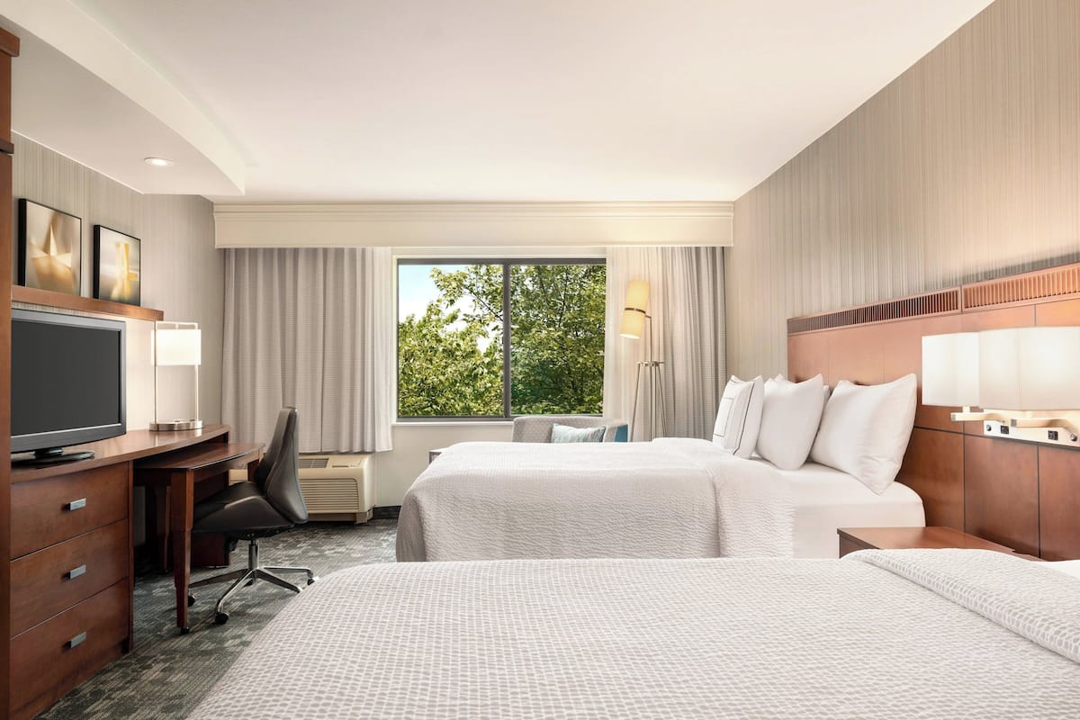 A hotel room with two beds, a desk with a TV, a chair, and a window with curtains.