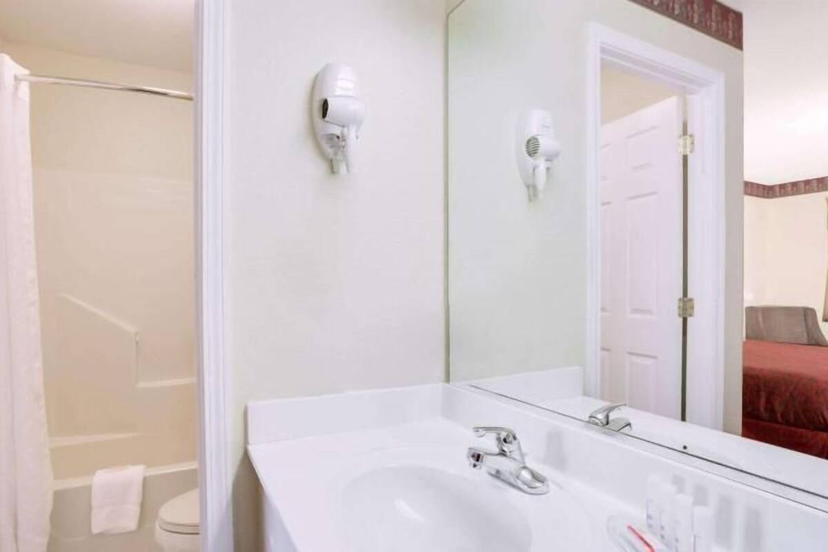 A hotel bathroom with a large mirror, a sink, a shower, and a toilet.