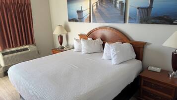 A hotel room with a large bed, wooden headboard, white bedding, two bedside lamps, a telephone, and a wall-mounted air conditioner.