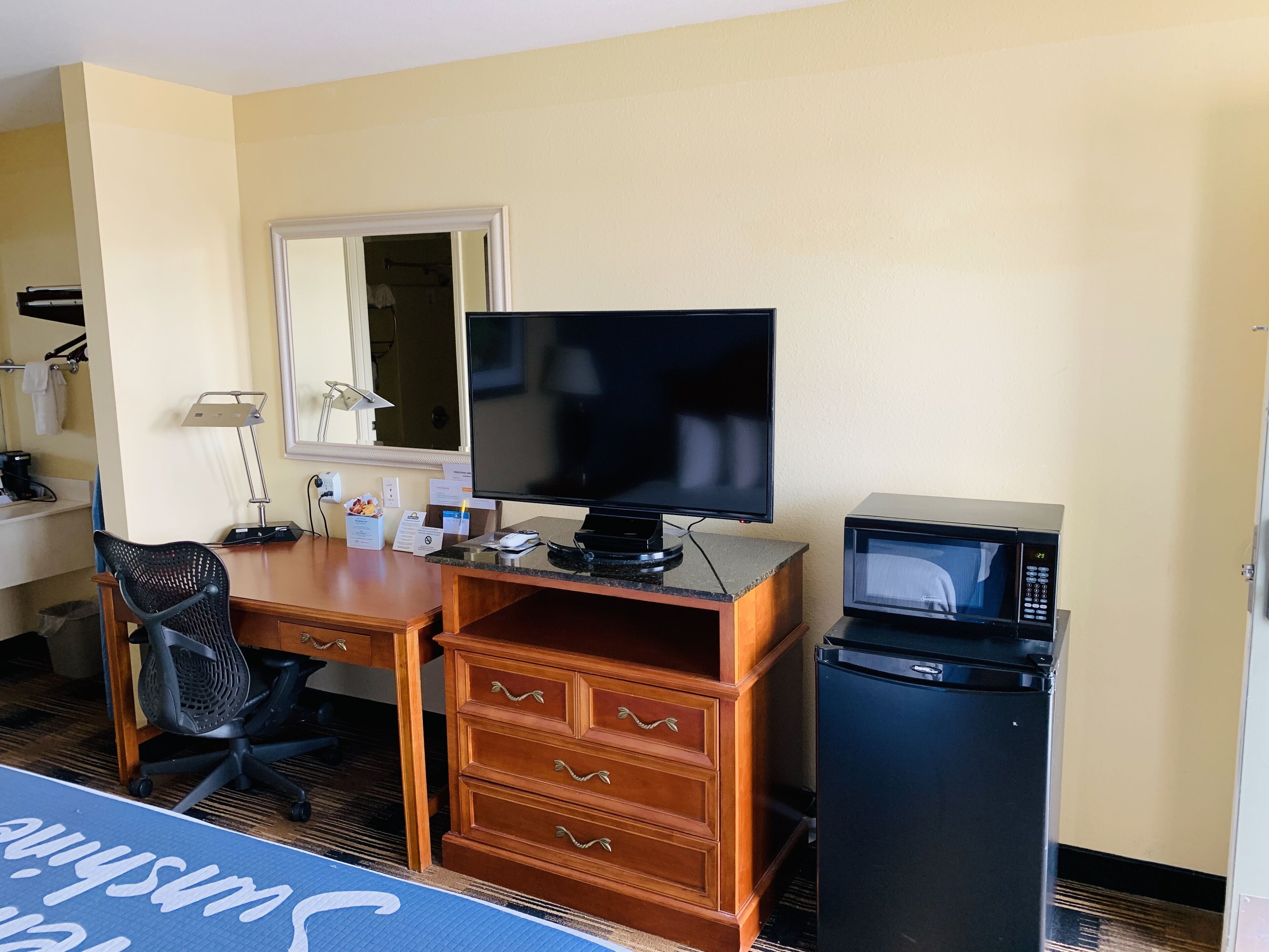 Habitación de hotel con escritorio de madera, televisión, microondas, silla y cómoda.