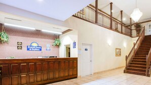 A reception area with a wooden reception desk, a sign for Days Inn & Suites, a staircase, and a chandelier. - Days Inn by Wyndham Trumann AR (Trumann)