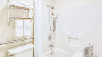Une salle de bain comprenant des toilettes, une douche avec un pommeau de douche amovible, une baignoire équipée d’une barre d’appui et une étagère contenant des articles de toilette.