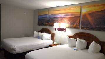 A hotel room with two beds, a nightstand with a lamp, and a wall-mounted phone.