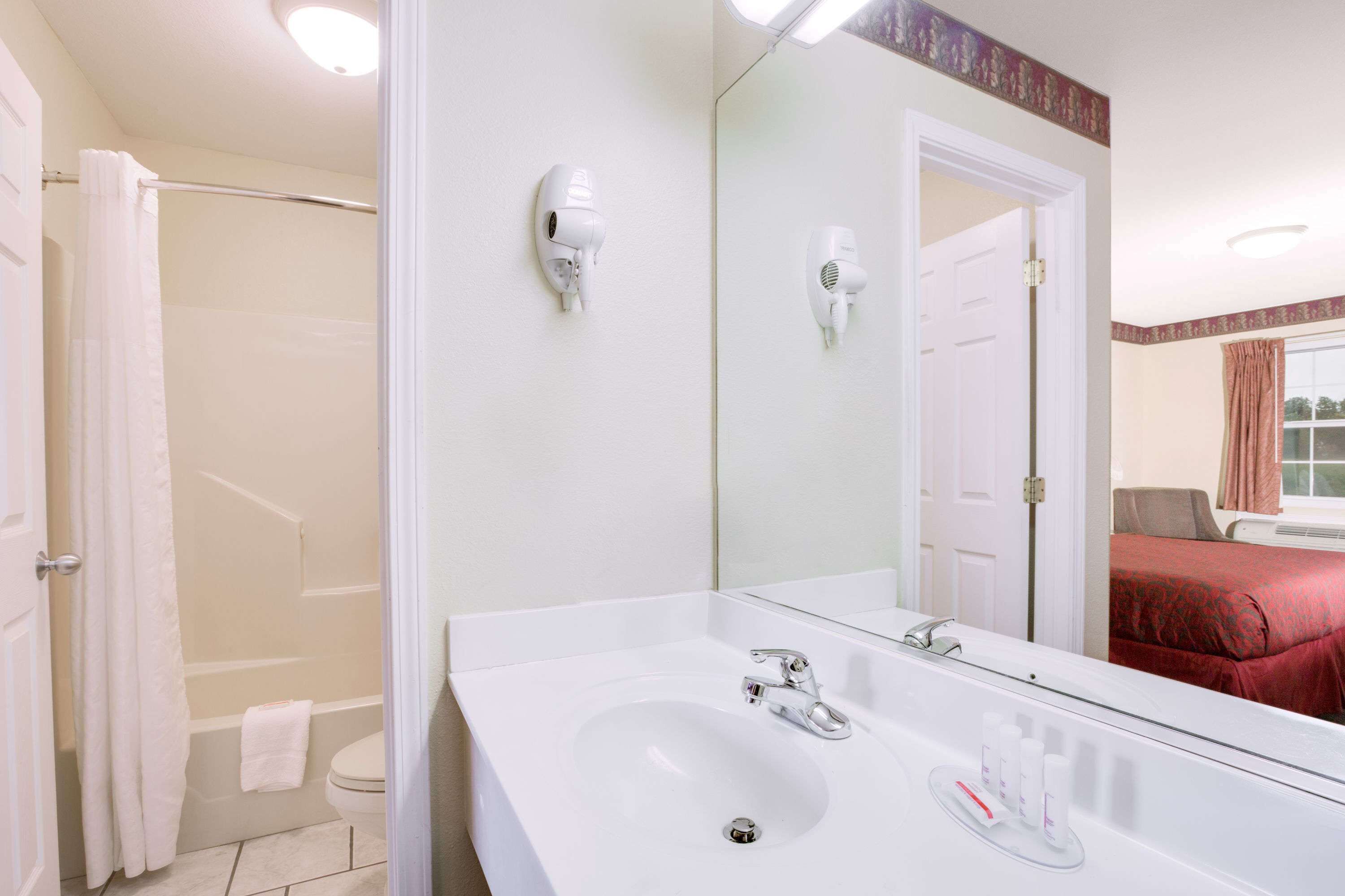 Un bagno con lavandino bianco, specchio e due asciugacapelli montati a parete.