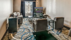 A hotel room with a sofa, armchairs, a coffee table, a TV, and a patterned carpet. - Holiday Inn Longview - North by IHG (Longview)
