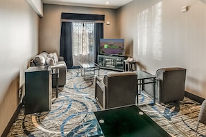 A hotel room with a sofa, armchairs, a coffee table, a TV, and a patterned carpet. - Holiday Inn Longview - North by IHG (Longview)