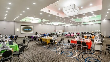 Sala de conferência com várias mesas, cadeiras e máquinas de costura, equipada com um projetor e uma tela grande exibindo o logotipo VIVITEK.