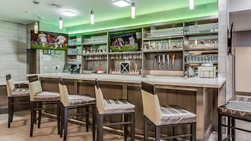 A bar area with a long counter, multiple stools, and shelves stocked with glasses and bottles.