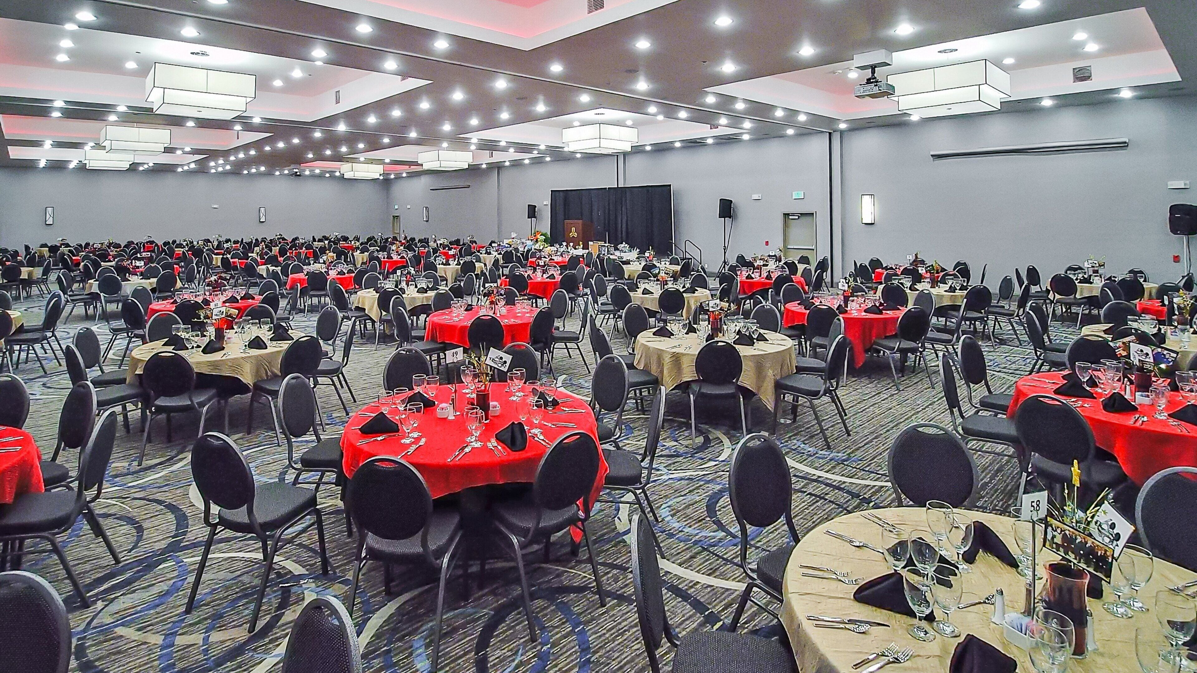 A large conference room with multiple round tables, each set with chairs and table settings.