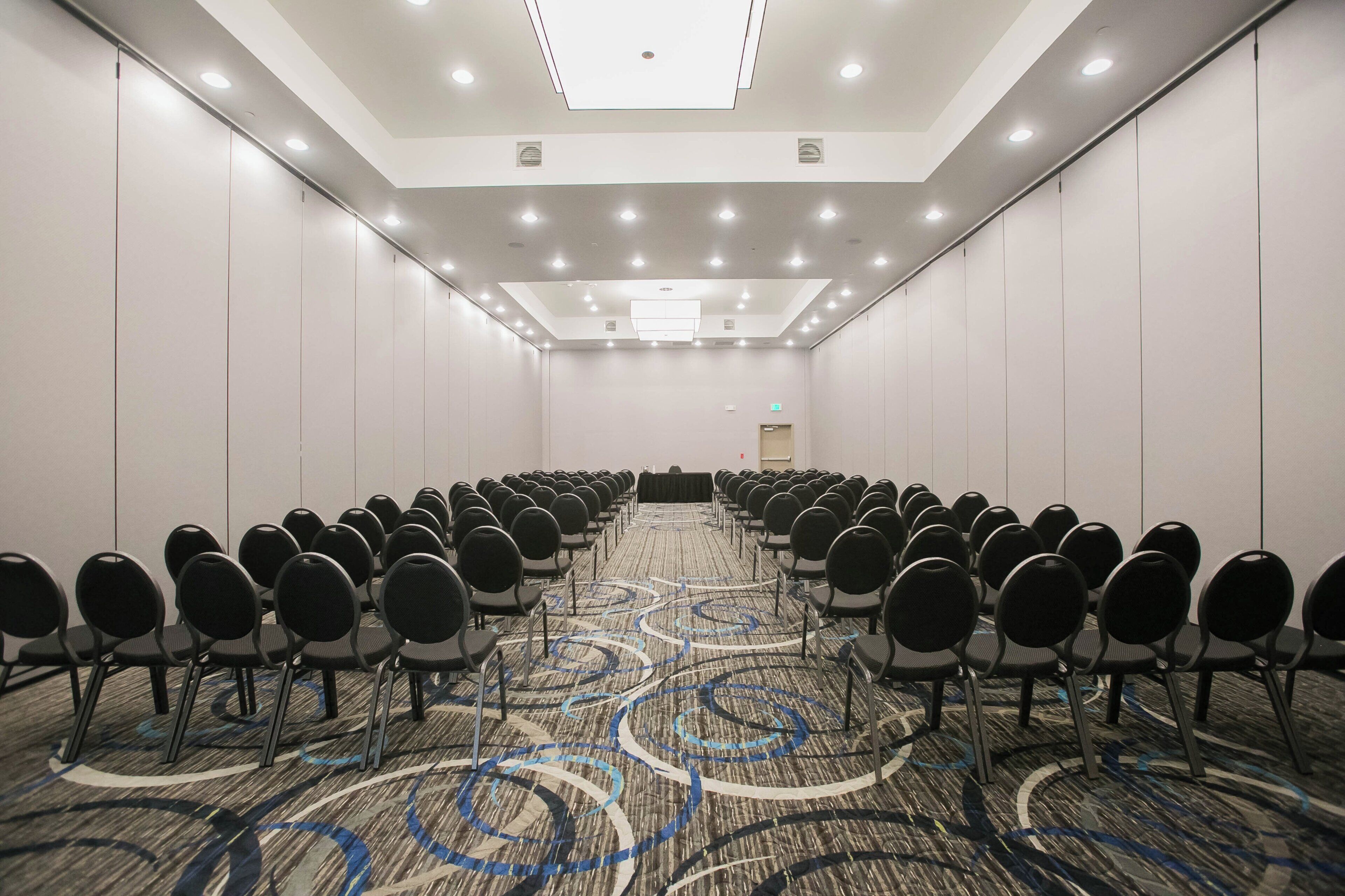 A conference room with rows of chairs, a patterned carpet, and a ceiling with recessed lighting.