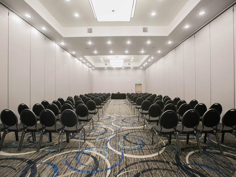 A conference room with rows of chairs, a patterned carpet, and a ceiling with recessed lighting.