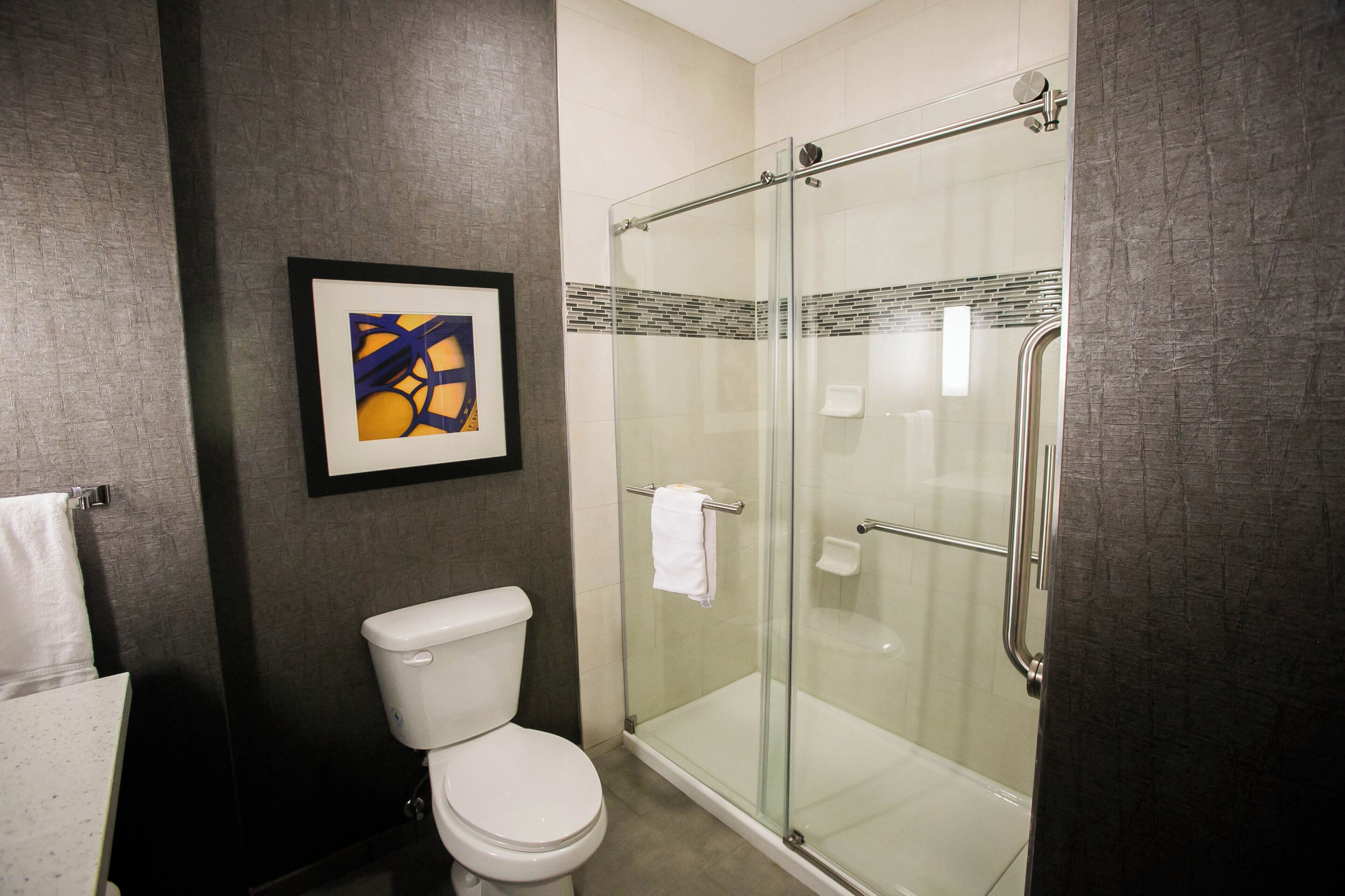 A bathroom with a toilet, a glass shower enclosure, and a framed abstract artwork on the wall.