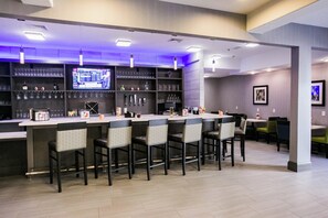 A bar area with a long counter, multiple bar stools, and a television screen displaying a menu. - Holiday Inn Longview - North by IHG (Longview)