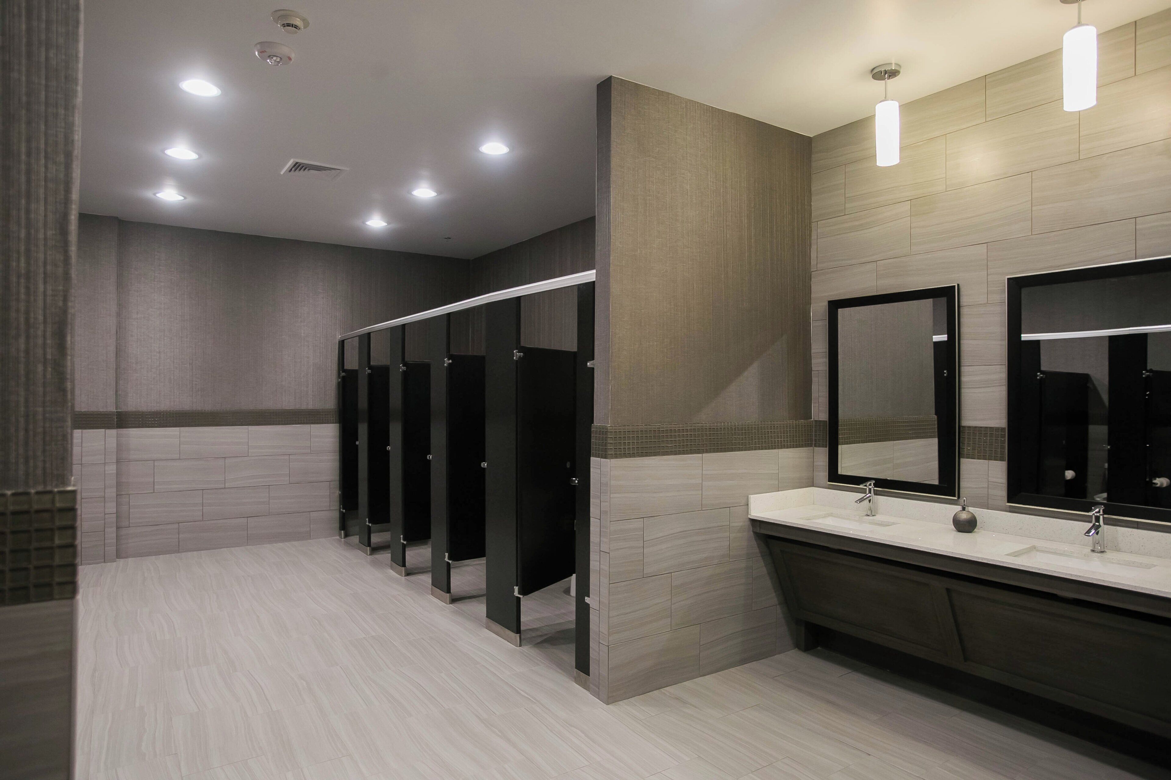 Des toilettes modernes dotées de plusieurs cabines, d’un meuble-lavabo avec un miroir et d’un éclairage encastré au plafond.