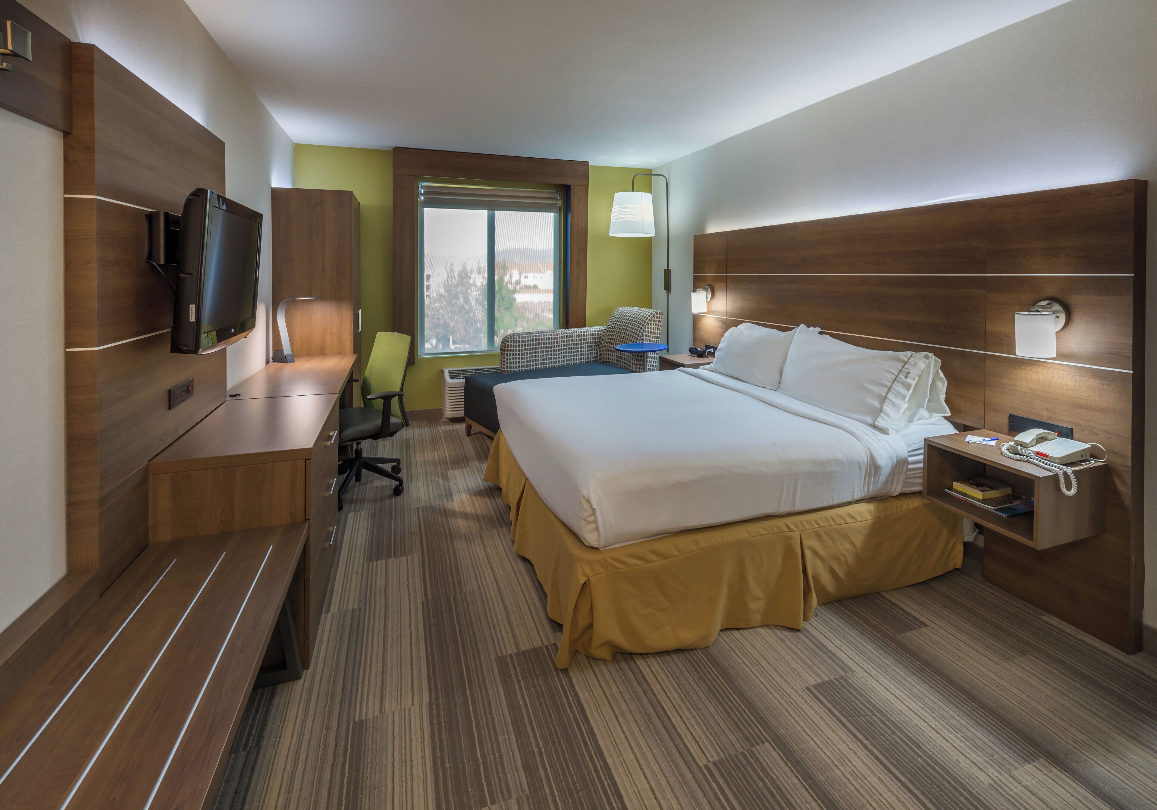 A hotel room with a bed, desk, chair, television, and a window with a view.