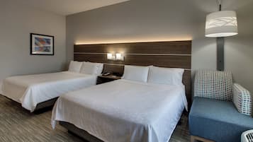 Ett hotellrum med två sängar, ett nattduksbord, en lampa, en stol och en väggmonterad lampa.