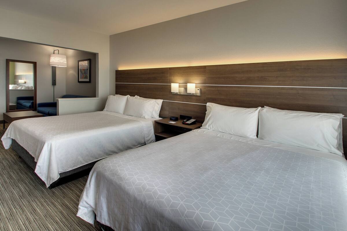 Habitación de hotel con dos camas, una mesita de noche con lámpara, un espejo y una lámpara de pared.