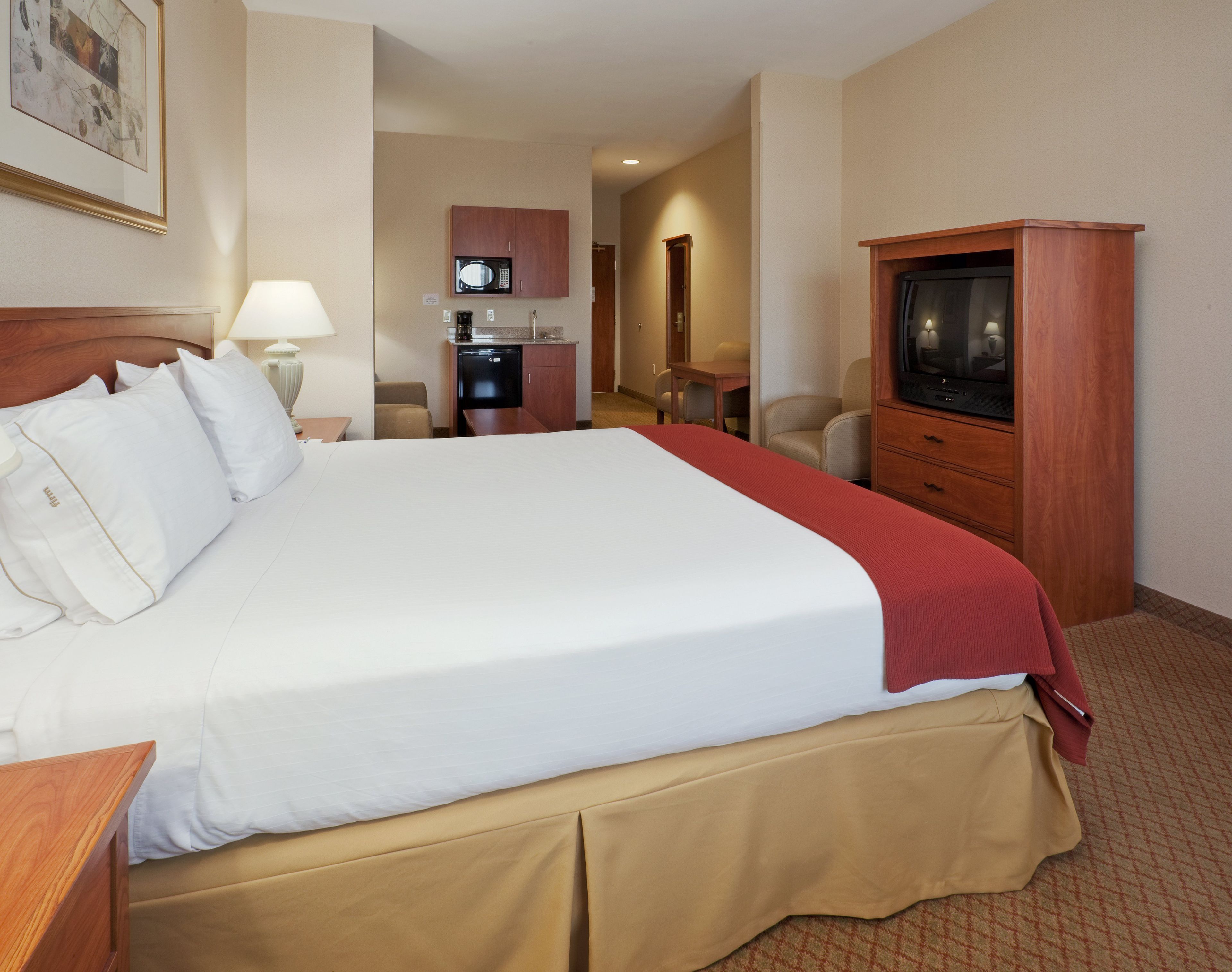 A hotel room with a large bed, a television, a desk, and a kitchenette.