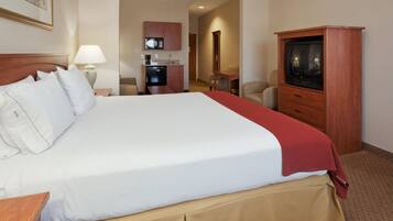 A hotel room with a large bed, a television, a desk, and a kitchenette.