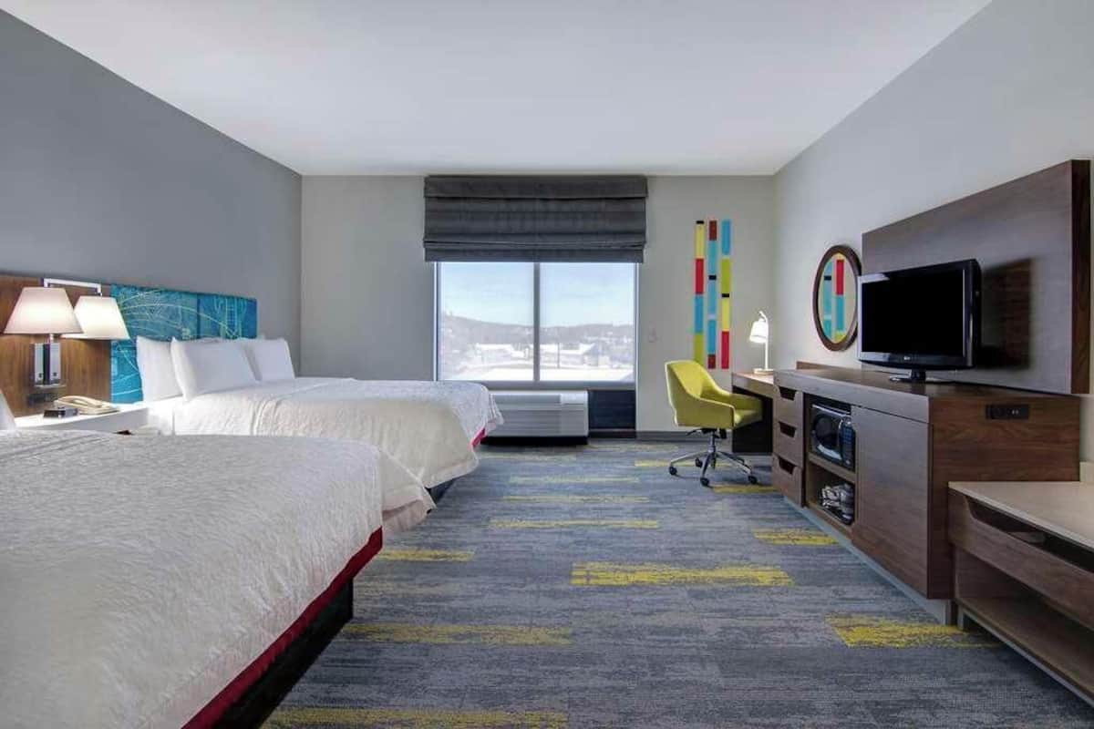 A hotel room with two beds, a desk with a TV, a chair, and a large window.