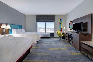Une chambre d’hôtel avec deux lits, un bureau avec une télévision, une chaise et une grande fenêtre.