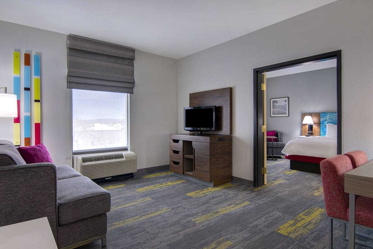A hotel room with a bed, a TV, a desk, a chair, and a window with a view.