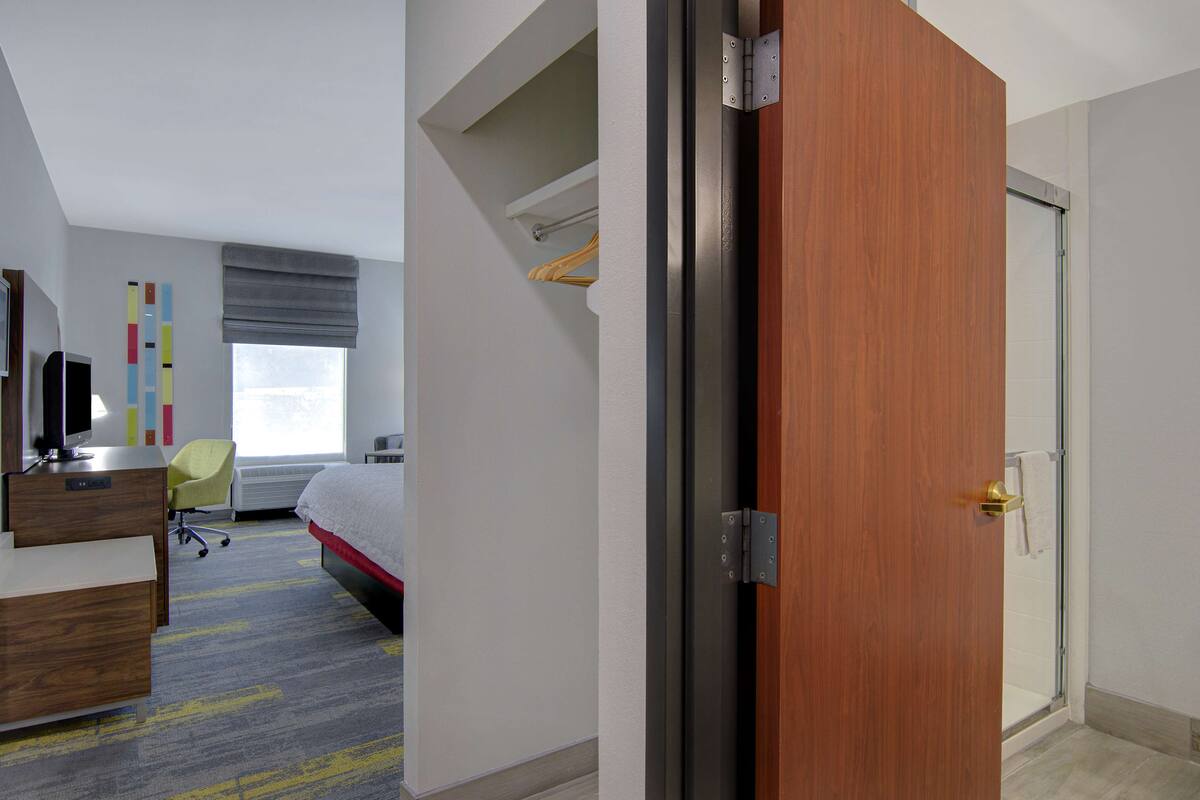 A hotel room with a bed, a desk, a chair, a wardrobe, and a bathroom with a shower.