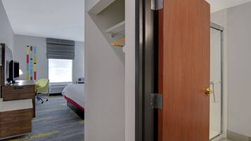 A hotel room with a bed, a desk, a chair, a wardrobe, and a bathroom with a shower.
