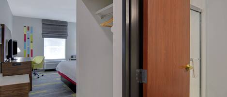 A hotel room with a bed, a desk, a chair, a wardrobe, and a bathroom with a shower.