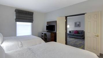 Une chambre d’hôtel avec deux lits, une télévision, un canapé et une porte donnant sur une autre pièce.