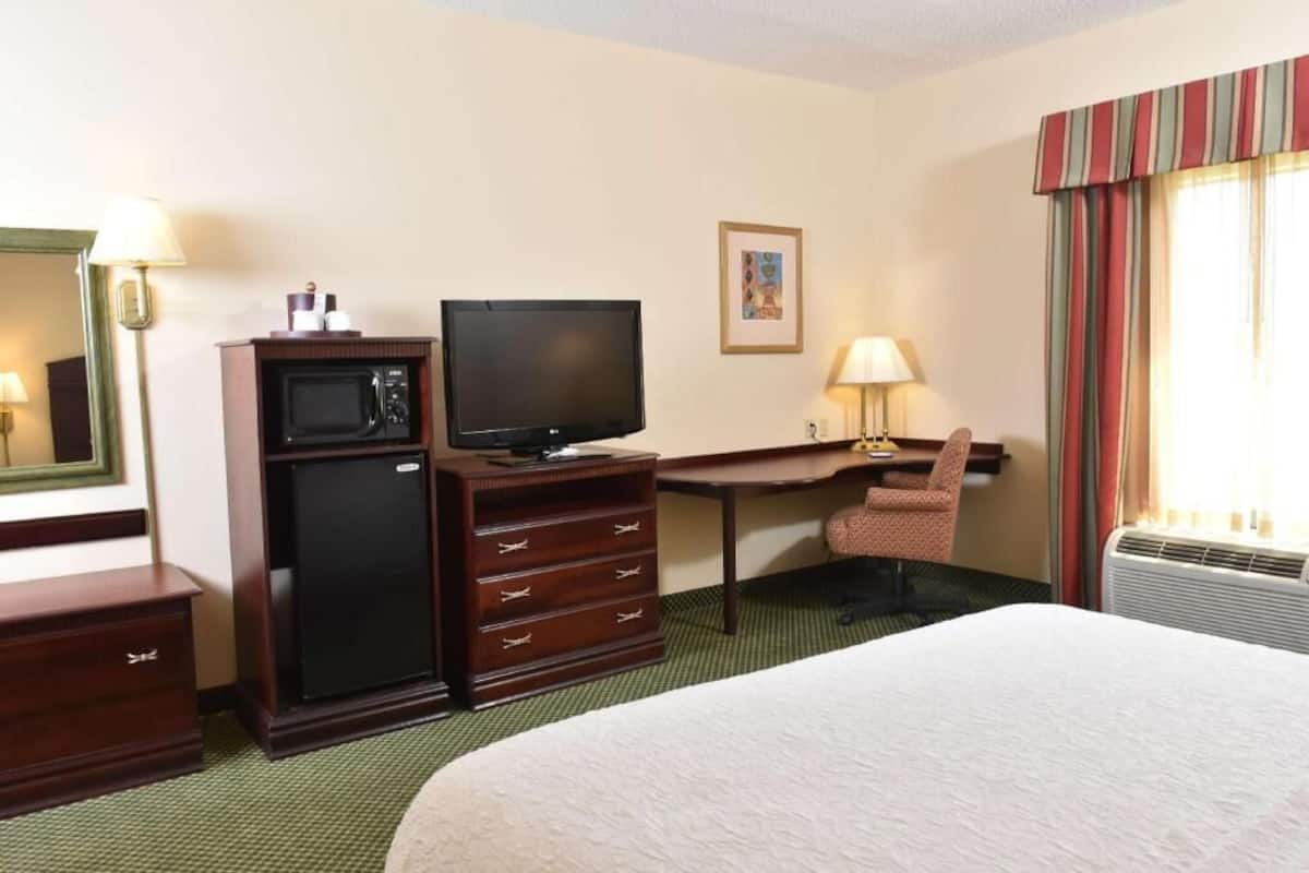 A hotel room with a bed, a desk with a computer, a television, a microwave, a dresser, and a chair.