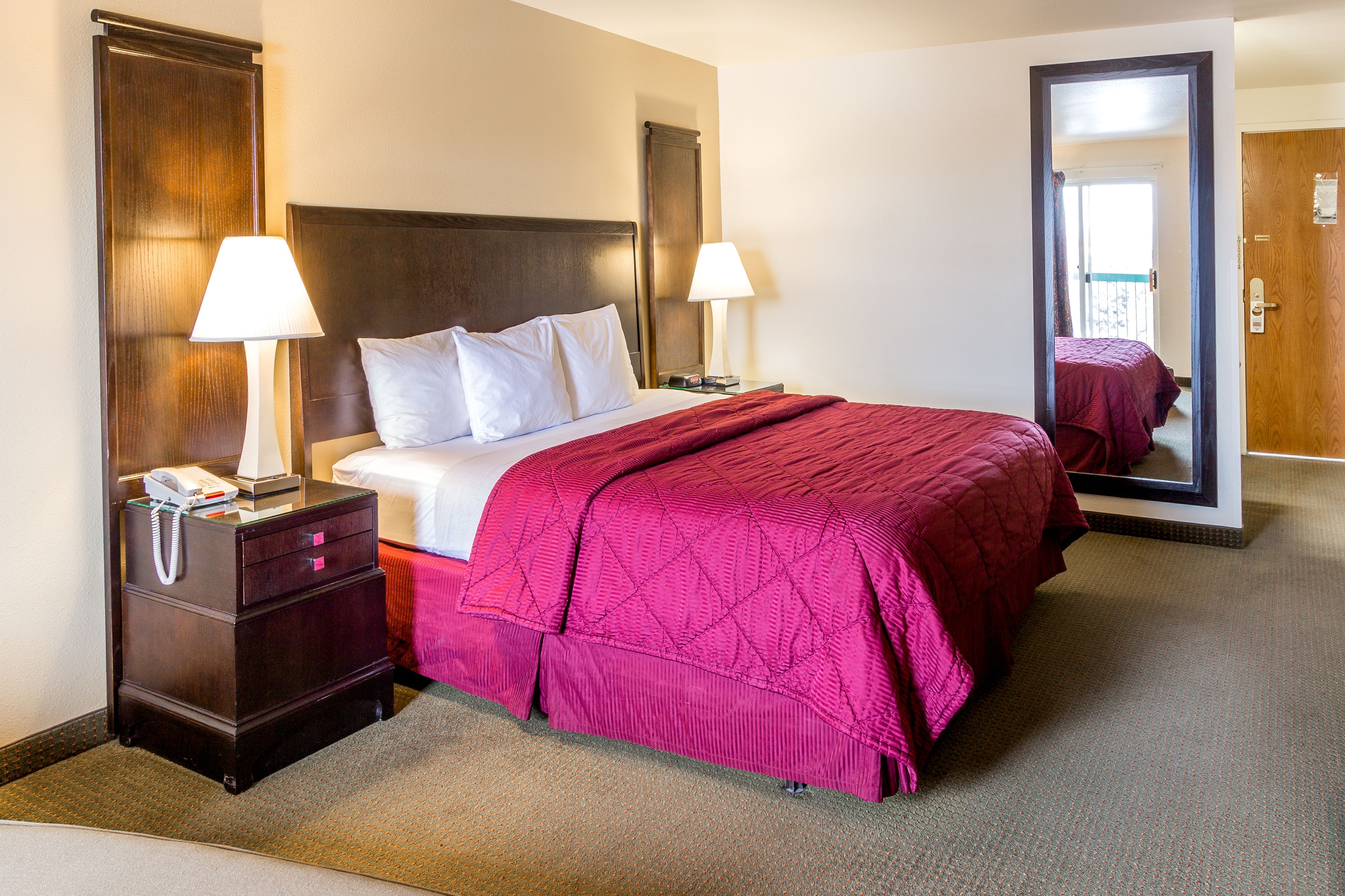 A hotel room with a bed, two bedside lamps, a nightstand with a phone, and a mirror.