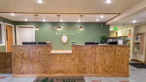Una recepción con diseño de madera, el cartel de Cedar Inn y un área de recepción con pared verde y luces en el techo.