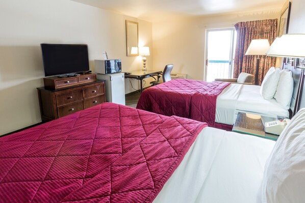 A hotel room with two beds, a desk, a television, and a small kitchenette.