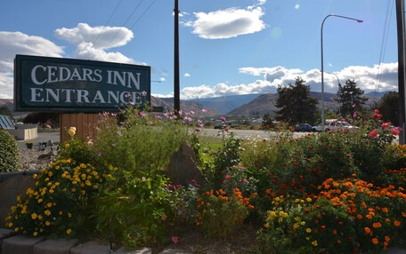 A sign for Cedar's Inn Entrance with a view of mountains and a parking lot in the background.
