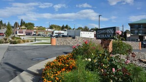 The entrance to Cedars Inn with a sign, a parking lot, and surrounding greenery.