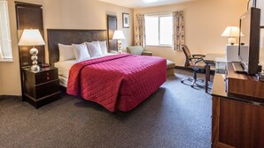 A hotel room with a large bed, two bedside tables with lamps, a desk with a chair, and a television.
