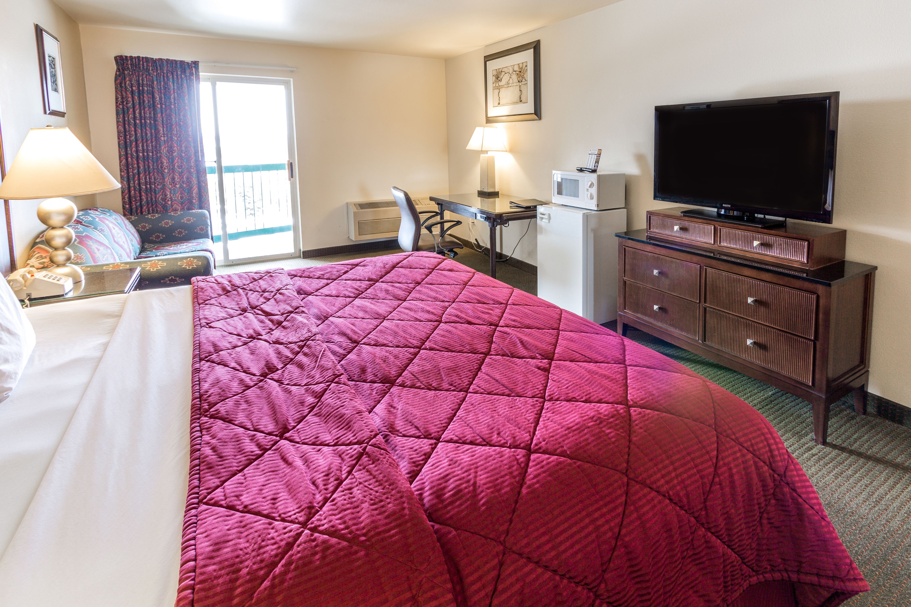 A hotel room with a large bed, a desk with a computer, a television, and a dresser.