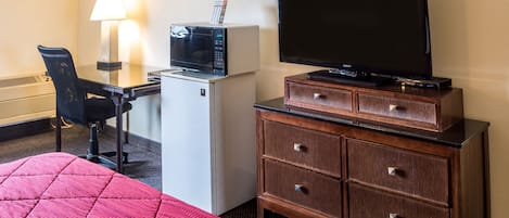 Una habitación de hotel con cama, escritorio con lámpara, microondas, televisor y cómoda.