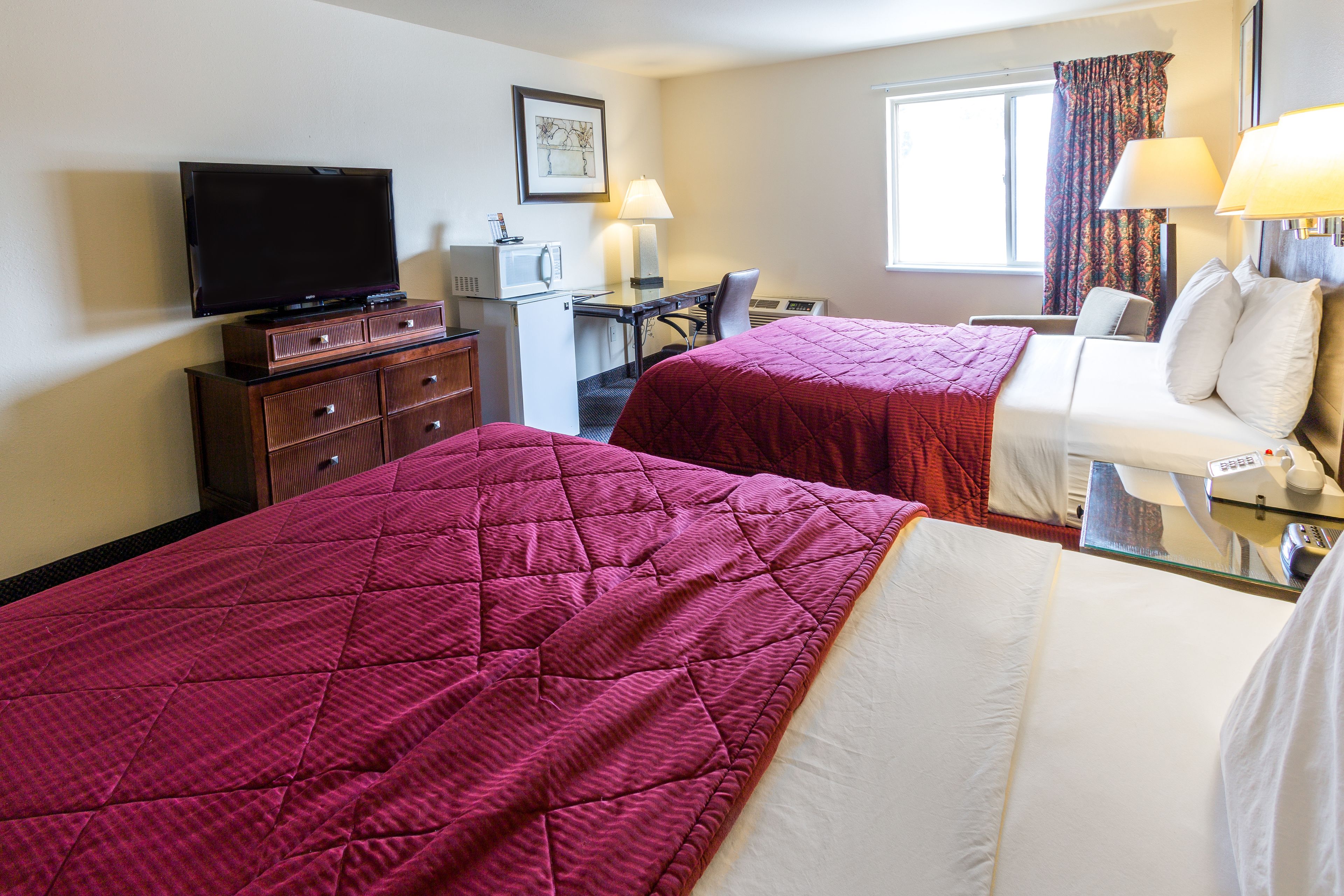 A hotel room with two beds, a desk with a computer, a television, and a window with curtains.