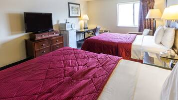 A hotel room with two beds, a desk with a computer, a television, and a window with curtains.