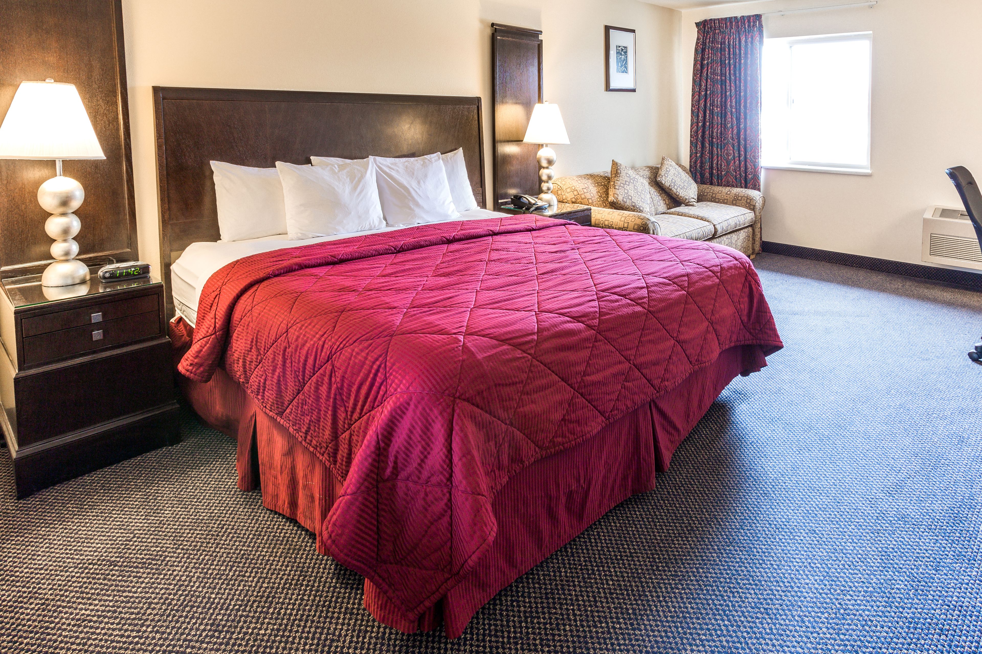 A hotel room with a large bed, two bedside tables with lamps, a chair, and a window with curtains.