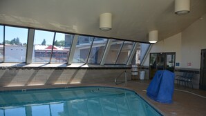 An indoor swimming pool with clear glass walls, a tiled floor, and a covered chair to the right.