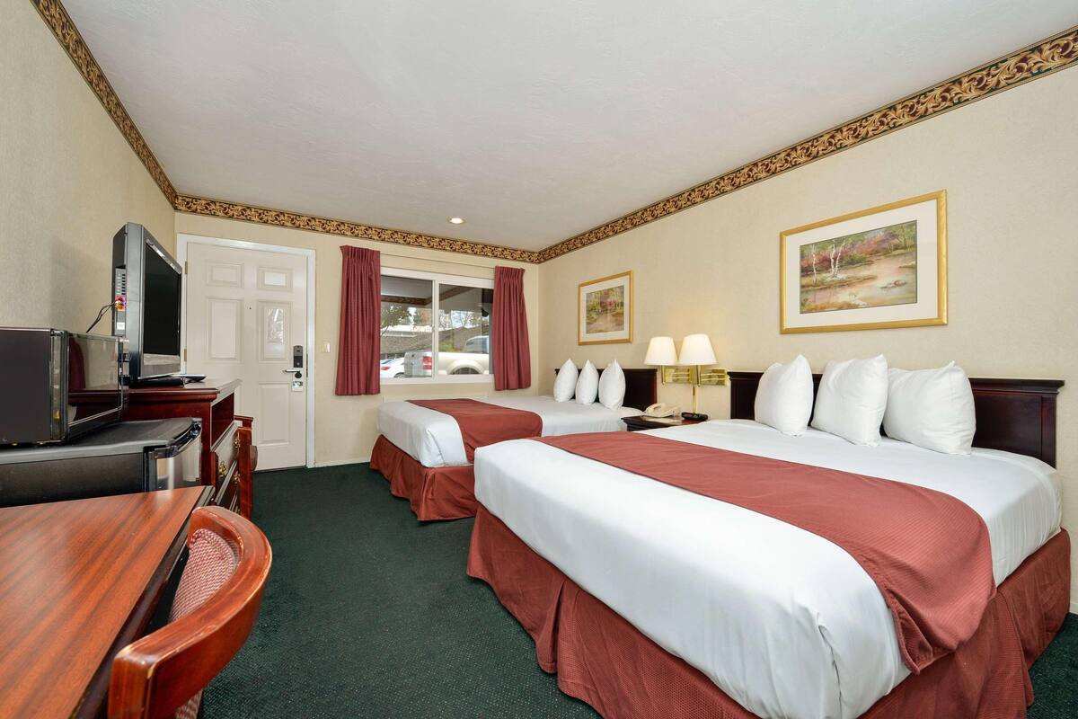 A hotel room with two beds, a desk with a TV, a door, and a window with curtains.