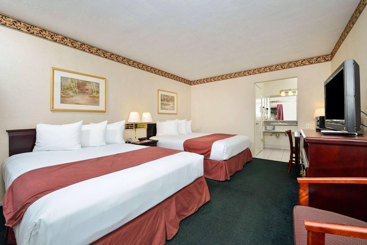 A hotel room with two beds, a desk, a television, and a mirror.