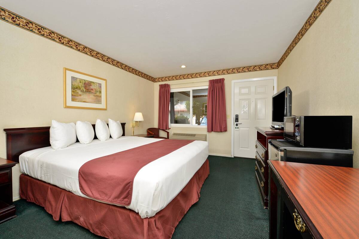 A hotel room with a large bed, a television, a desk, and a window with curtains.