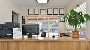 A reception desk with a printer, computer monitor, and a potted plant. - Americas Best Value Inn Sky Ranch Palo Alto (Palo Alto)